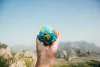 Hand holding a miniature globe against a mountainous landscape, representing global responsibility and environmental awareness.