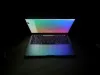 Open laptop glowing with a colorful screen in a dark room.