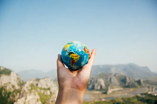 Hand holding a miniature globe against a mountainous landscape, representing global responsibility and environmental awareness.
